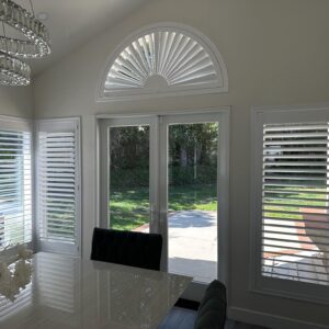 Large dining room with white plantation shutters or indoor shutters on the windows. A specialty shape shutter is above the door to the backyard.