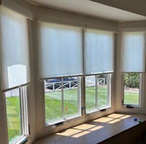 White roller shades on large living room windows.