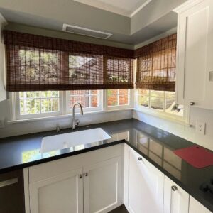 Brown woven shades on the window above a kitchen sink.